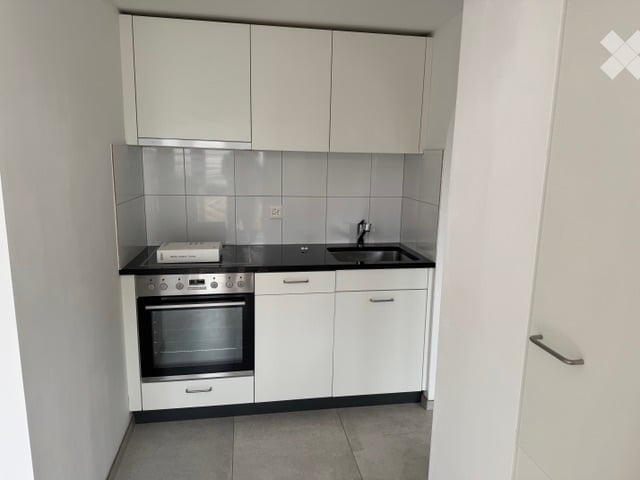 Modern kitchen with white cabinets, black countertops, and built-in oven. Features a sink and a small appliance on the counter.