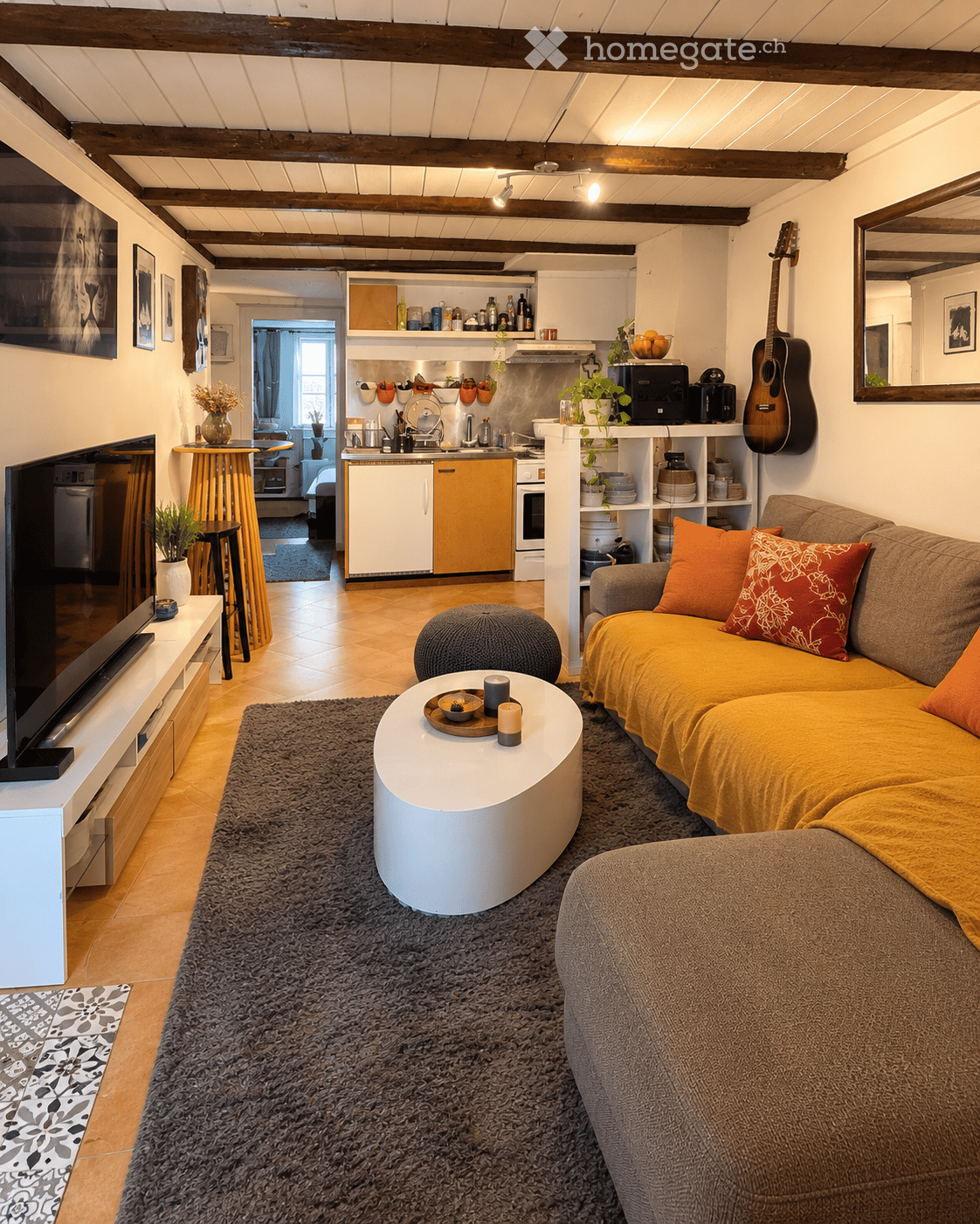 Cozy living room with a yellow sofa, white coffee table, grey rug, and a small kitchen area visible in the background. Features wooden beams on the ceiling, a guitar on the wall, and various decorative items.