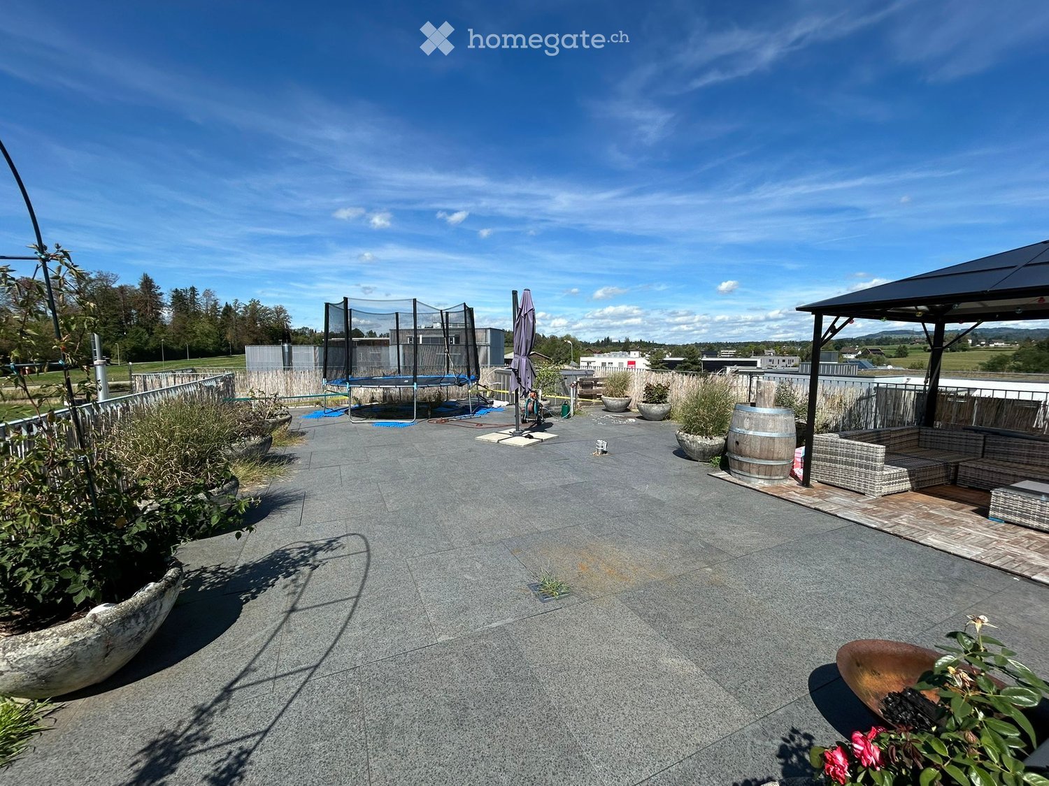 Outdoor patio with seating area, trampoline, and various potted plants.