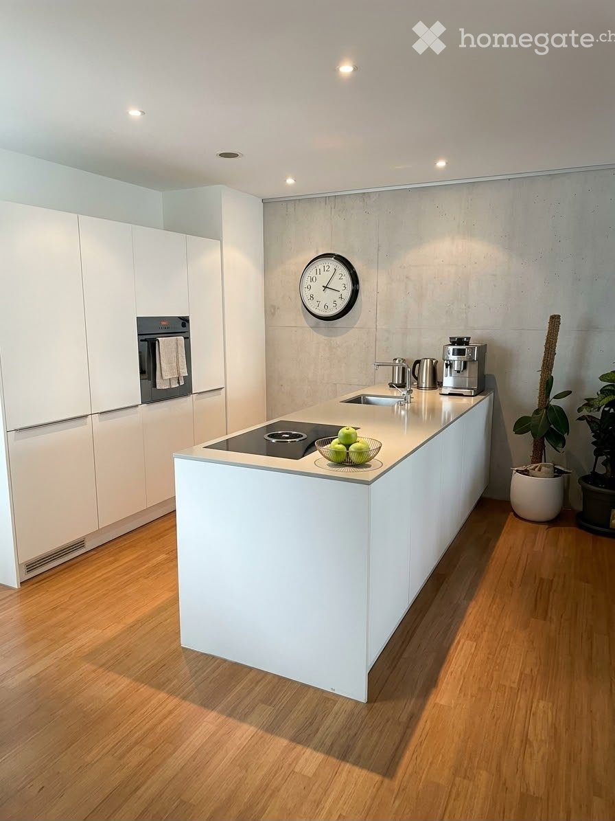 Modern kitchen with white cabinets, induction cooktop, sink, coffee maker, and a clock on the wall.