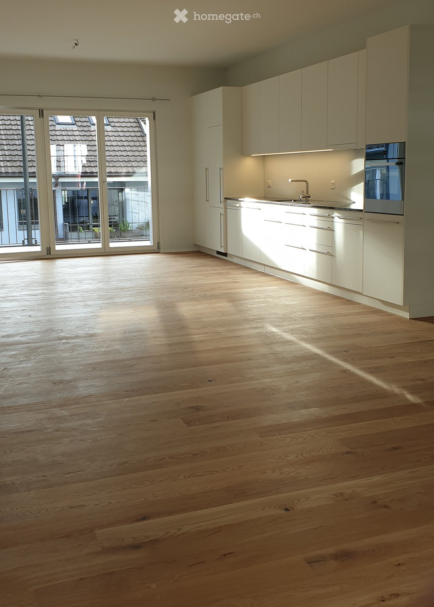 Empty kitchen with light wooden flooring, white cabinetry, and large sliding glass doors leading to a balcony.