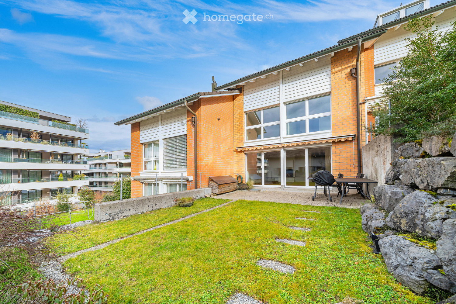 Garden area with a small lawn, patio furniture, and a modern building in the background.