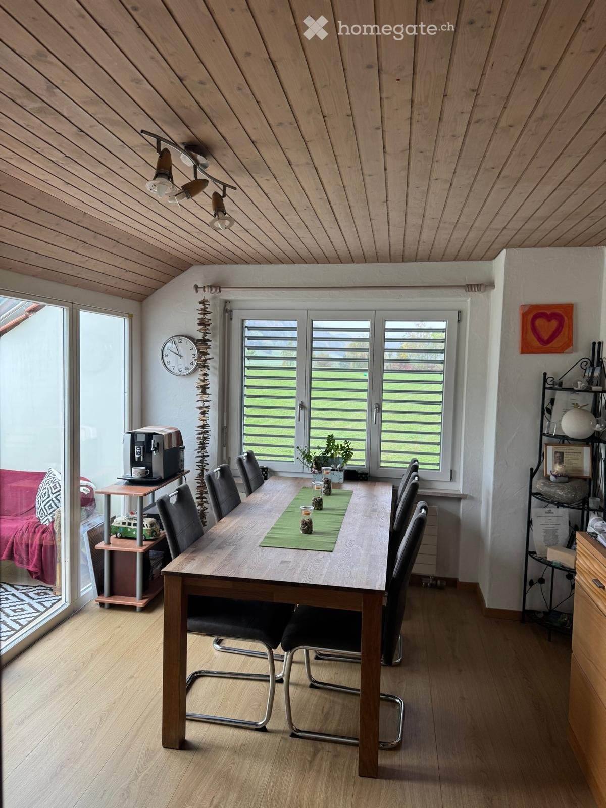 Bright, modern dining area with wooden table, black chairs, coffee machine, clock, and decorative items.
