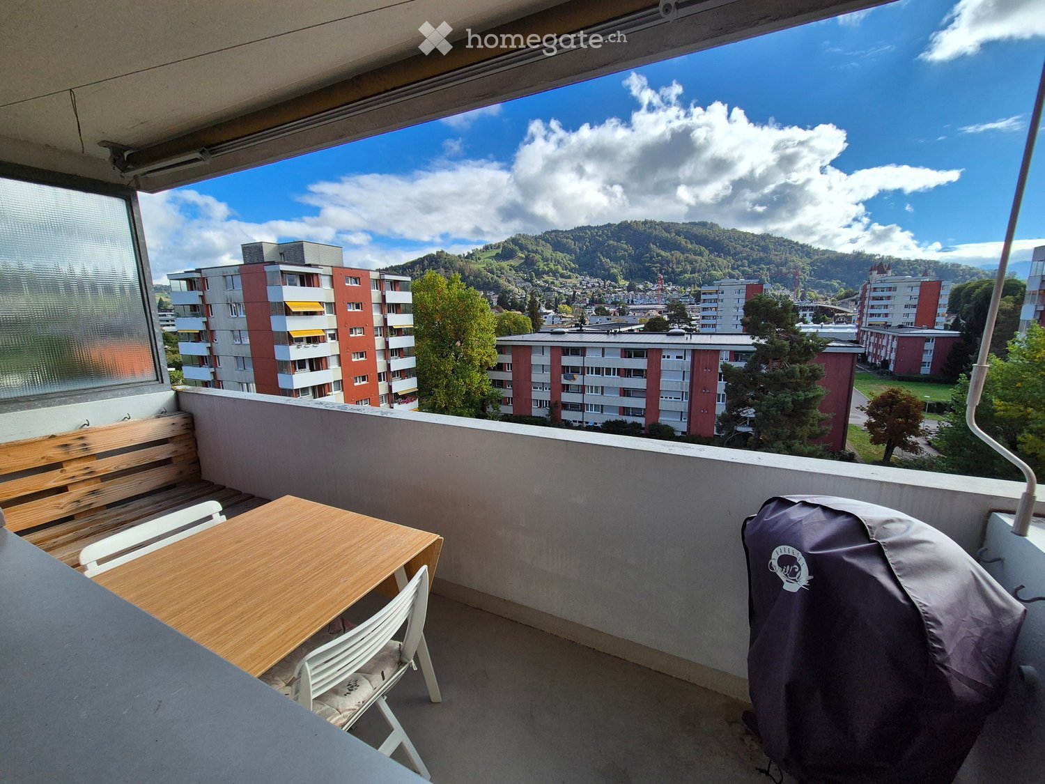 Balcony with wooden table, chairs, bench, and scenic mountain view.