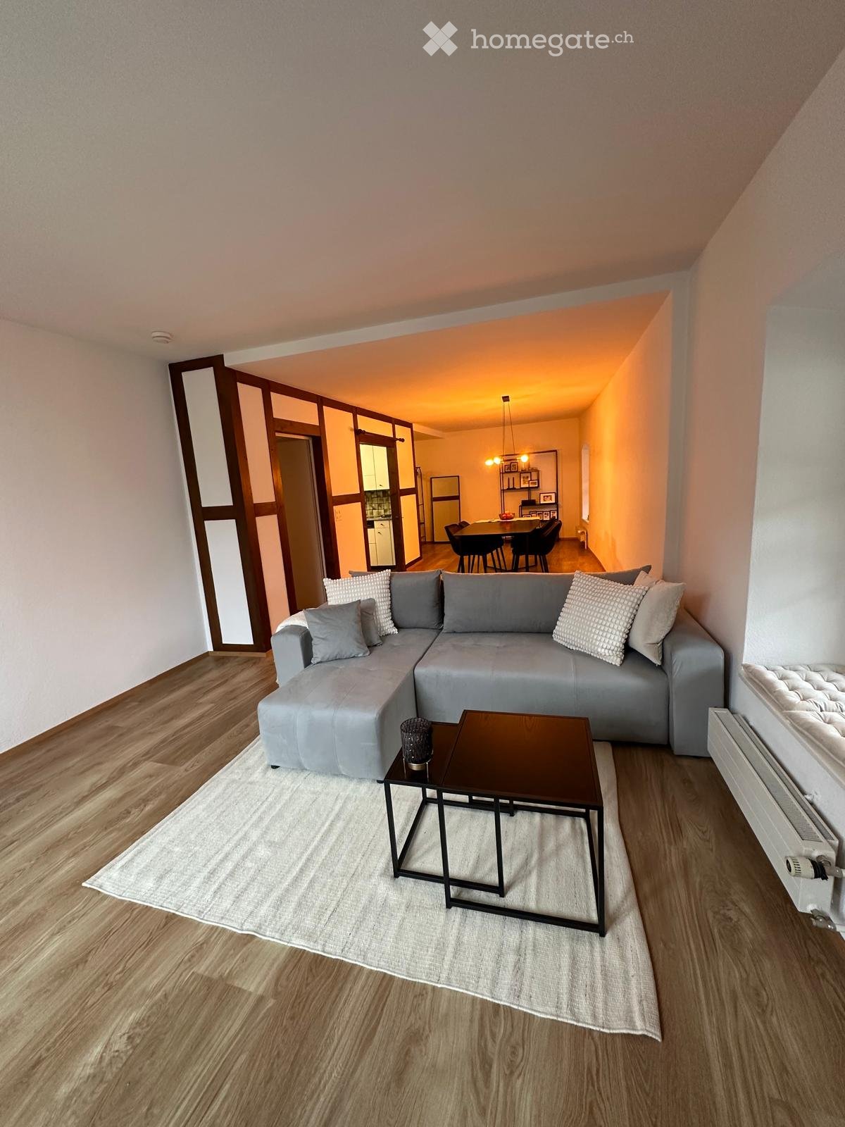 Modern living room with grey sectional sofa, coffee table, dining table, and chairs in the adjacent dining area.