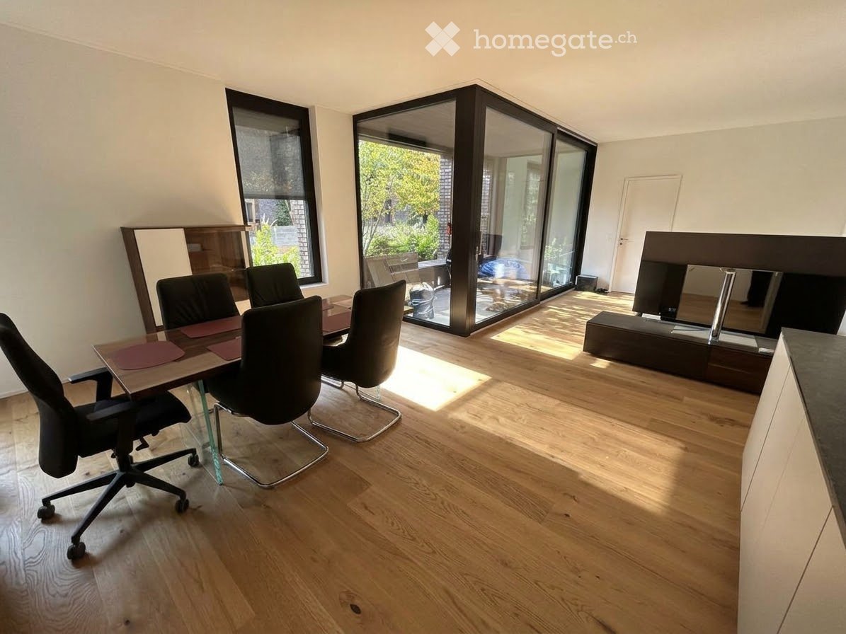 Bright room with wooden flooring, large windows, and sliding glass doors leading to a balcony. Includes a table with chairs and a screen.
