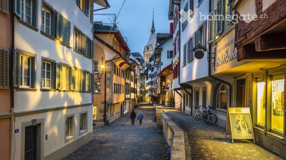 A charming European town street lined with colorful historic buildings, cobblestone pavement, and warm lighting from street lamps.