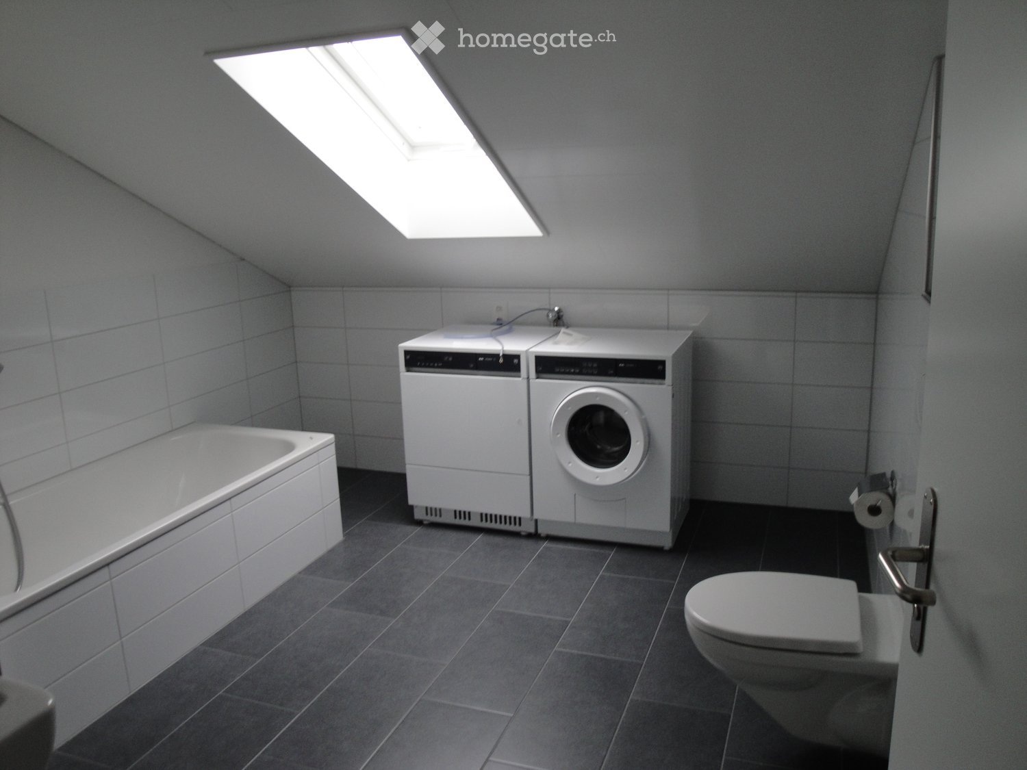 Modern bathroom with a bathtub, toilet, washing machine, and a skylight window providing natural light.