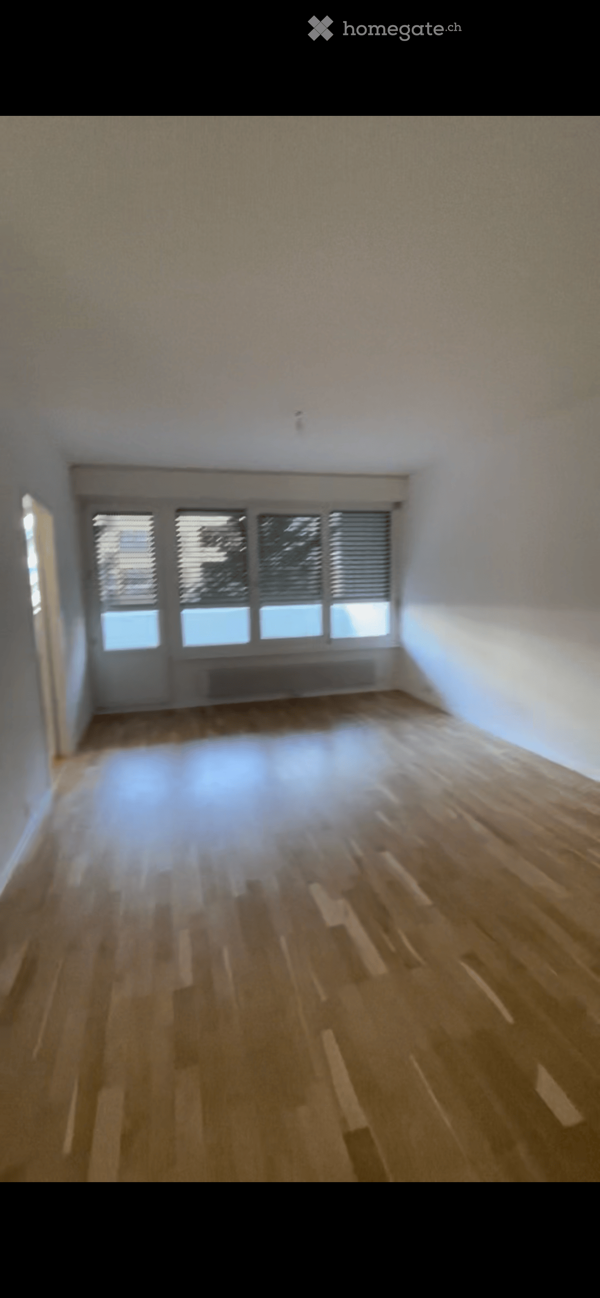 Empty room with wooden flooring, white walls, and large windows with blinds. No furniture or equipment present.