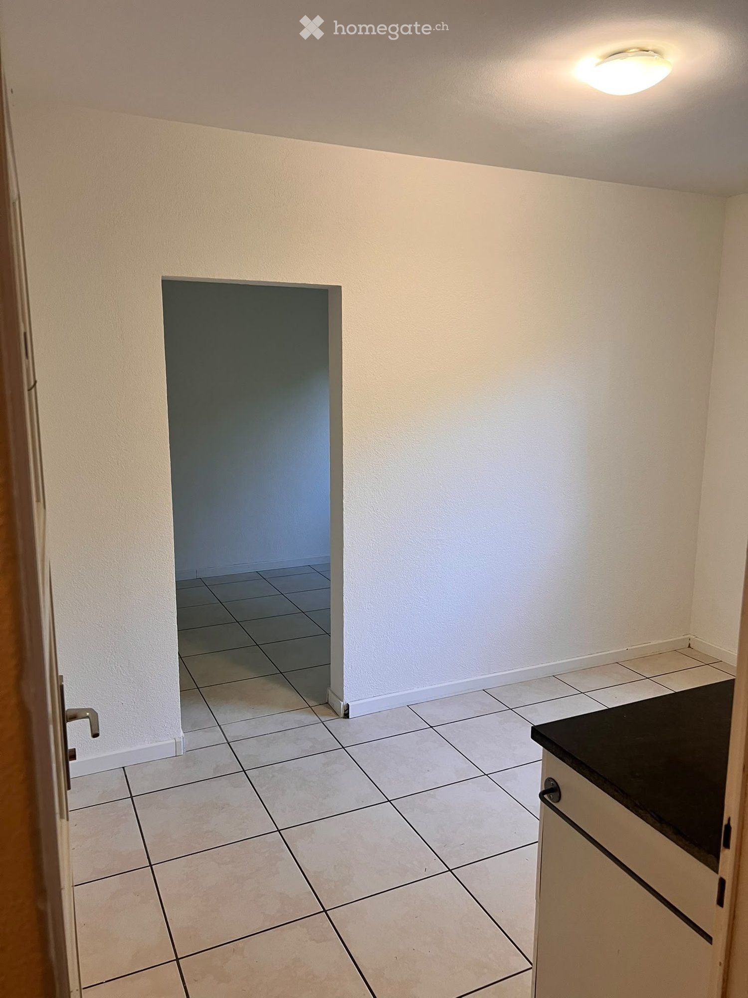 Empty room with tiled floor, white walls, and a small black countertop on the right side.