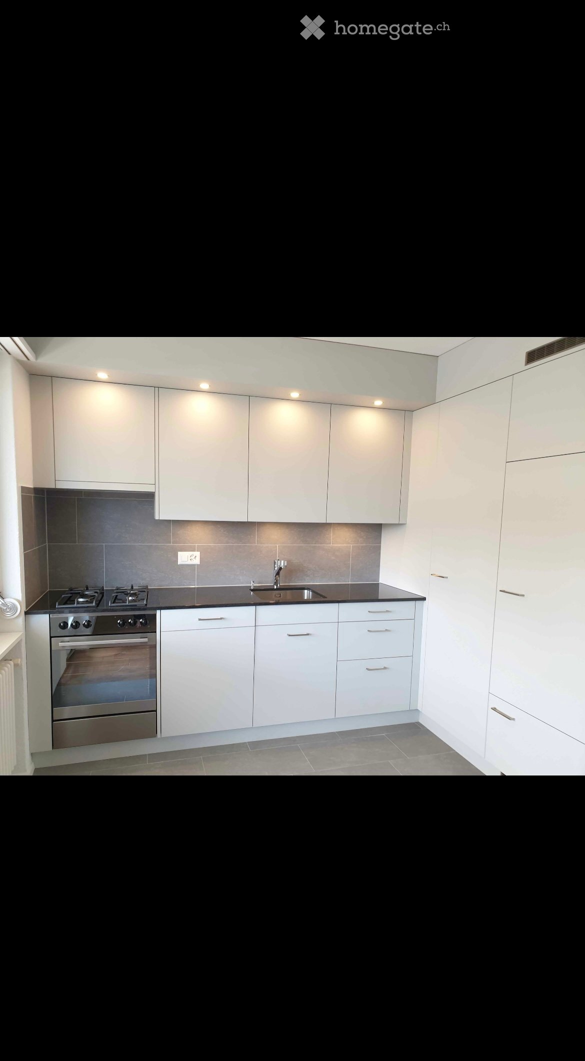 Modern kitchen with white cabinets, stainless steel oven, sink, and faucet, featuring a black countertop and gray tiled floor.