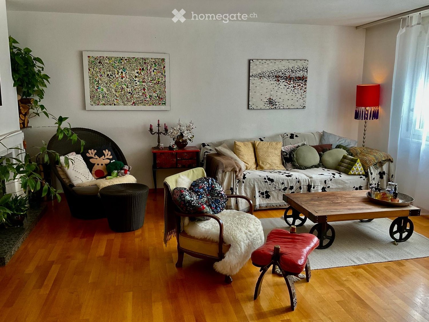 Living room with wooden flooring, a sofa with multiple cushions, a coffee table with wheels, a wooden side table, a floor lamp, and decorative items including a vase and candles.