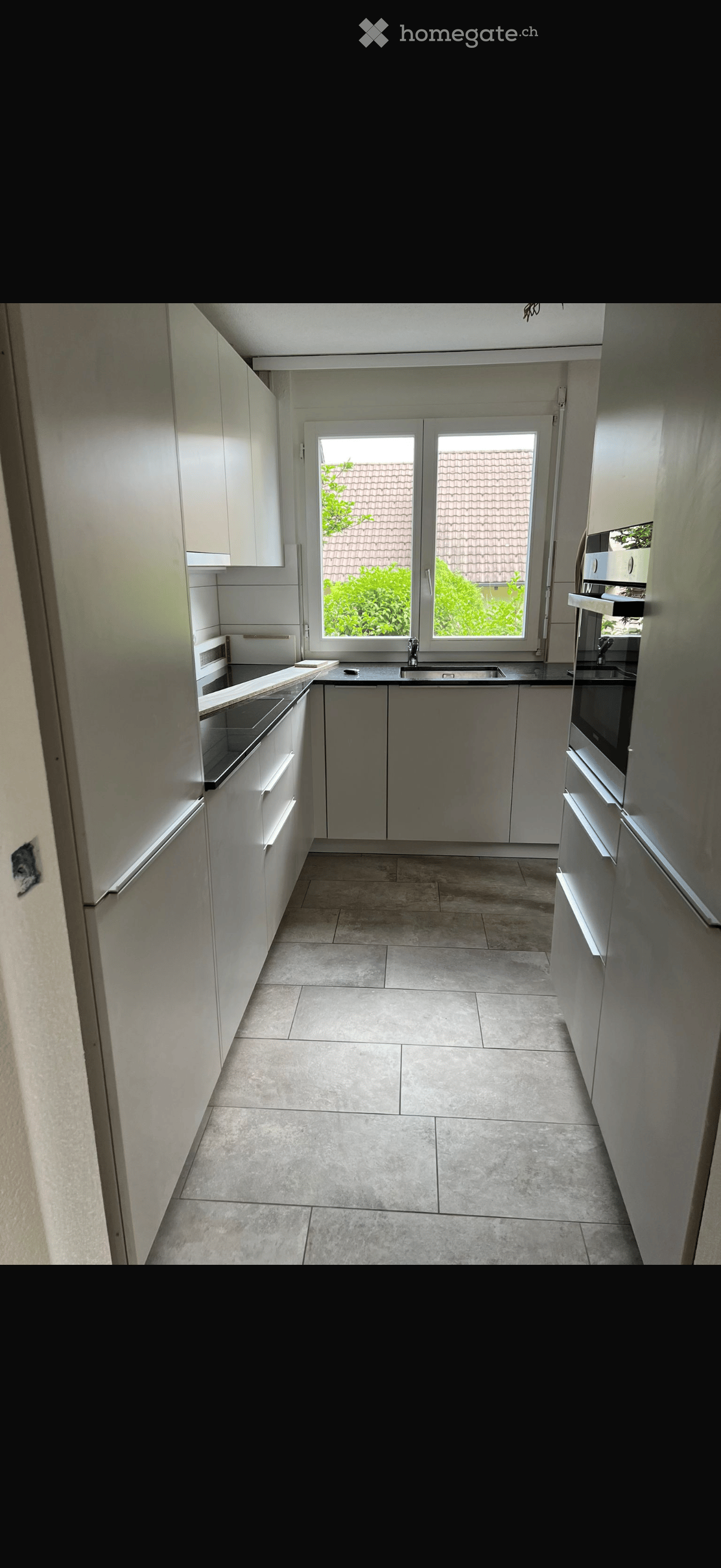Modern kitchen with white cabinets, stainless steel appliances, and a large window overlooking a garden.