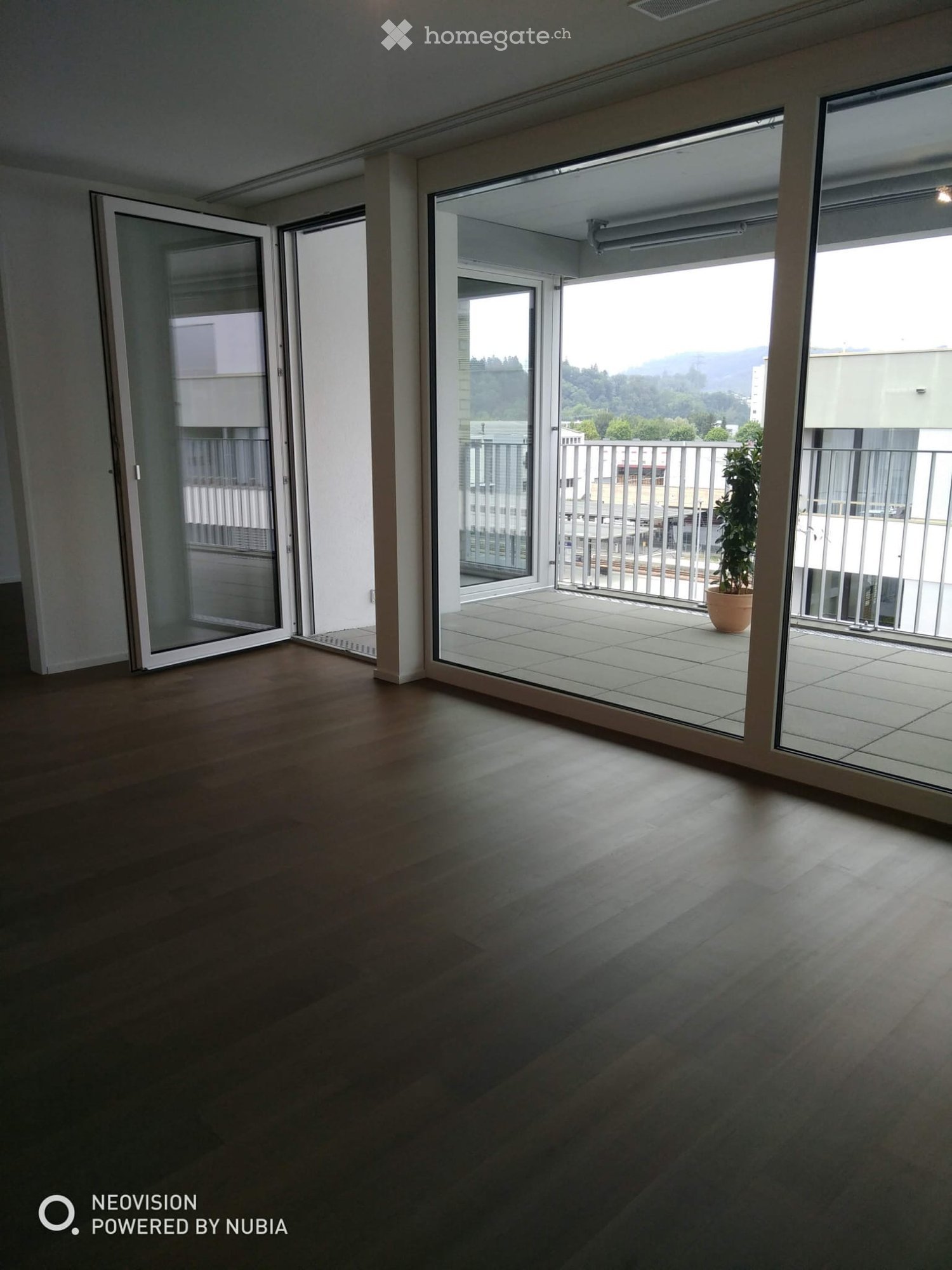 Empty room with wooden flooring and large sliding glass doors leading to a balcony with a potted plant.