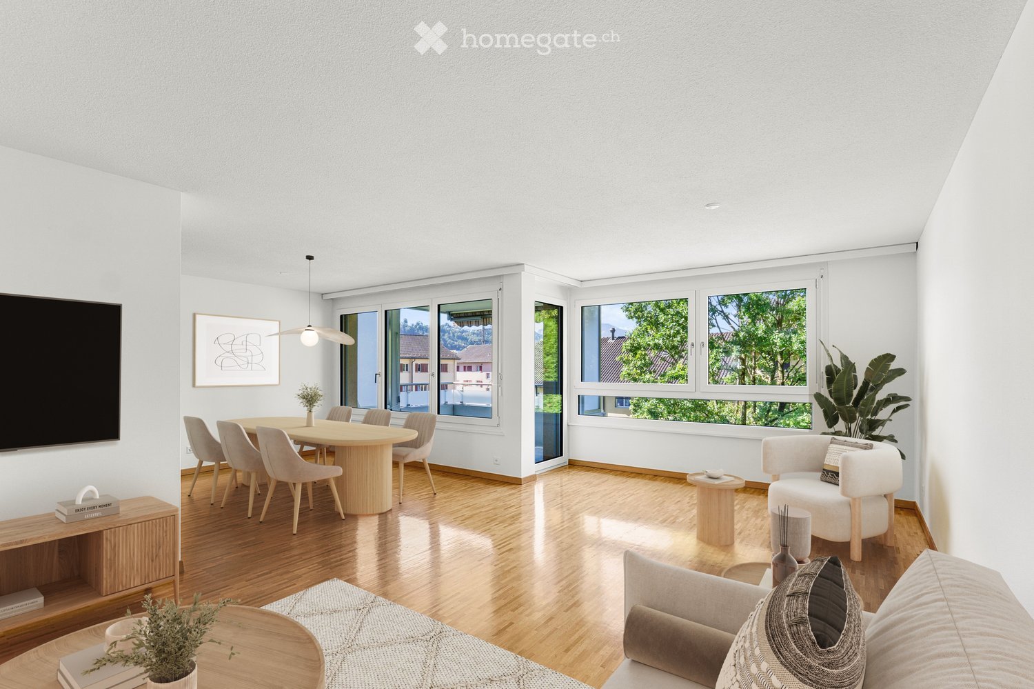Bright living room with wooden flooring, large windows, a sofa, coffee table, dining area with round table and chairs, pendant light, and decorative plants.