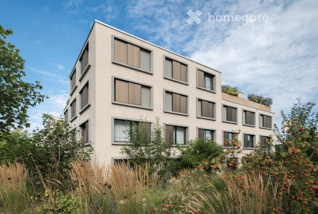 Modern multi-story building with large windows and shutters, surrounded by greenery and flowers.