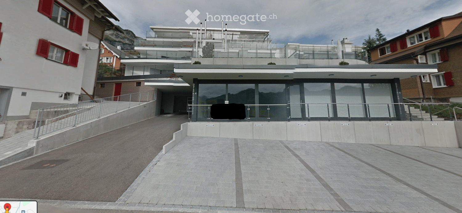 Modern multi-story building with glass balconies and raised ground floor entrance.
