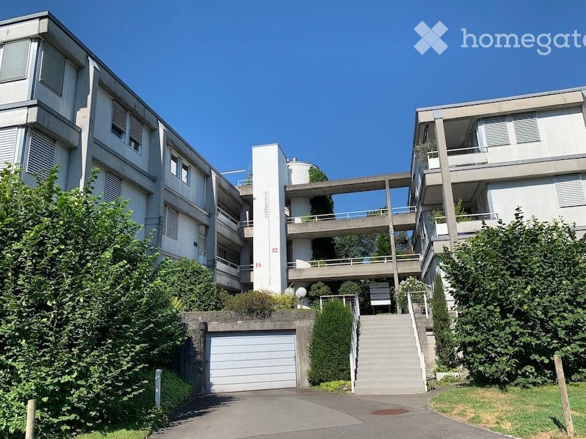 Modern multi-story residential building with white exterior, balconies, and a connected garage.