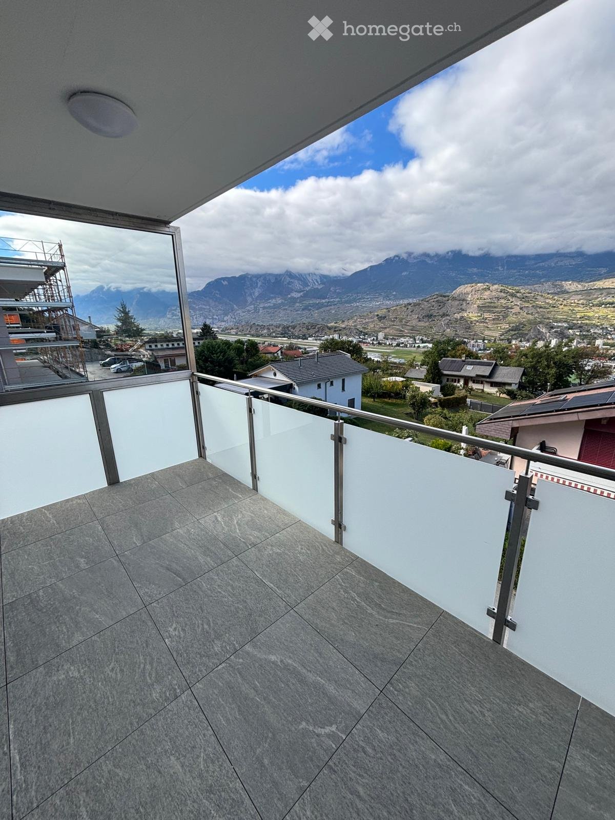Balcony with modern glass railing, tiled floor, and scenic mountain view.