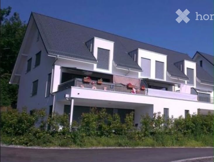 Modern two-story house with white exterior, grey roof, and a large balcony on the upper floor.