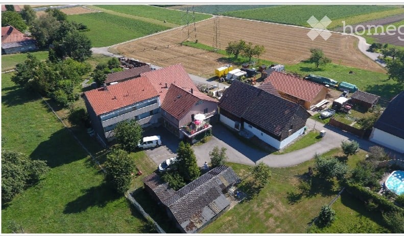 Aerial view of a residential complex with multiple houses, parking area, and a swimming pool in a rural setting.