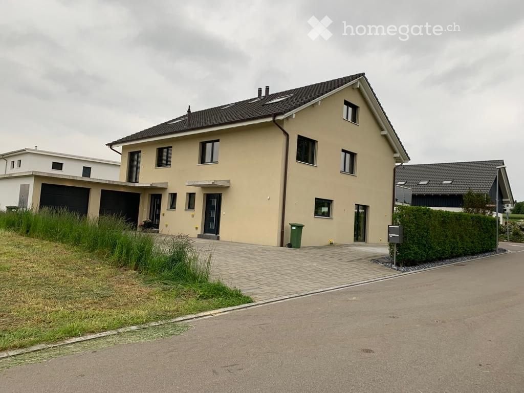 Two-story house with beige exterior, multiple windows, garage, and driveway.