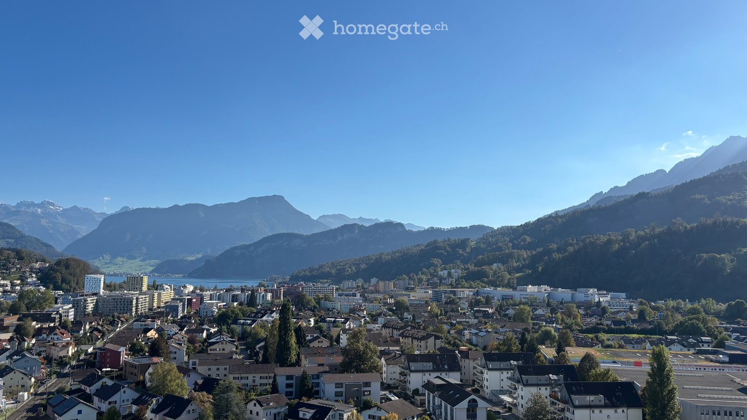 A panoramic view of a town nestled in a valley surrounded by mountains, with a lake visible in the distance.