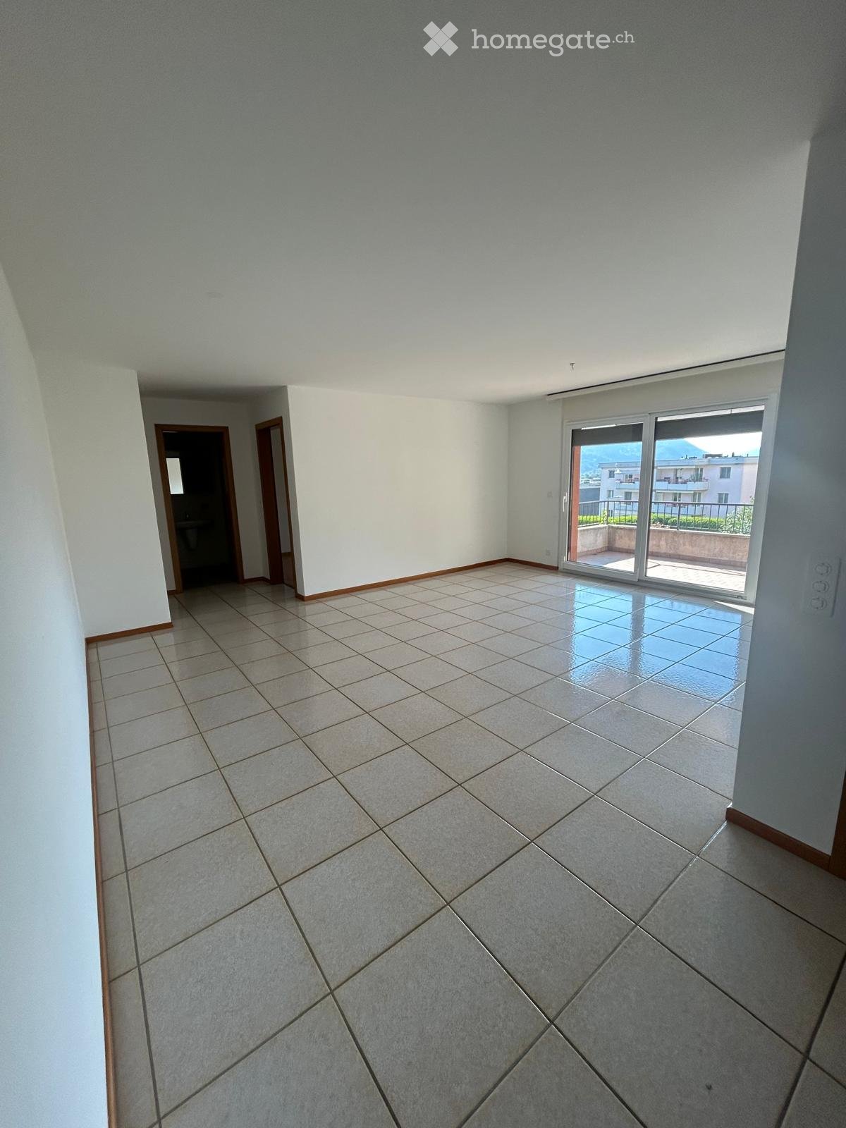 Empty room with tiled floor, white walls, and a sliding glass door leading to a balcony.
