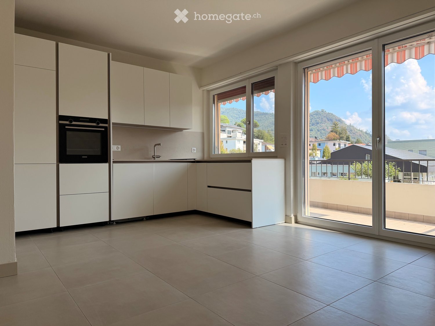 Modern kitchen with white cabinets, an oven, and a faucet, featuring large windows with scenic mountain views.