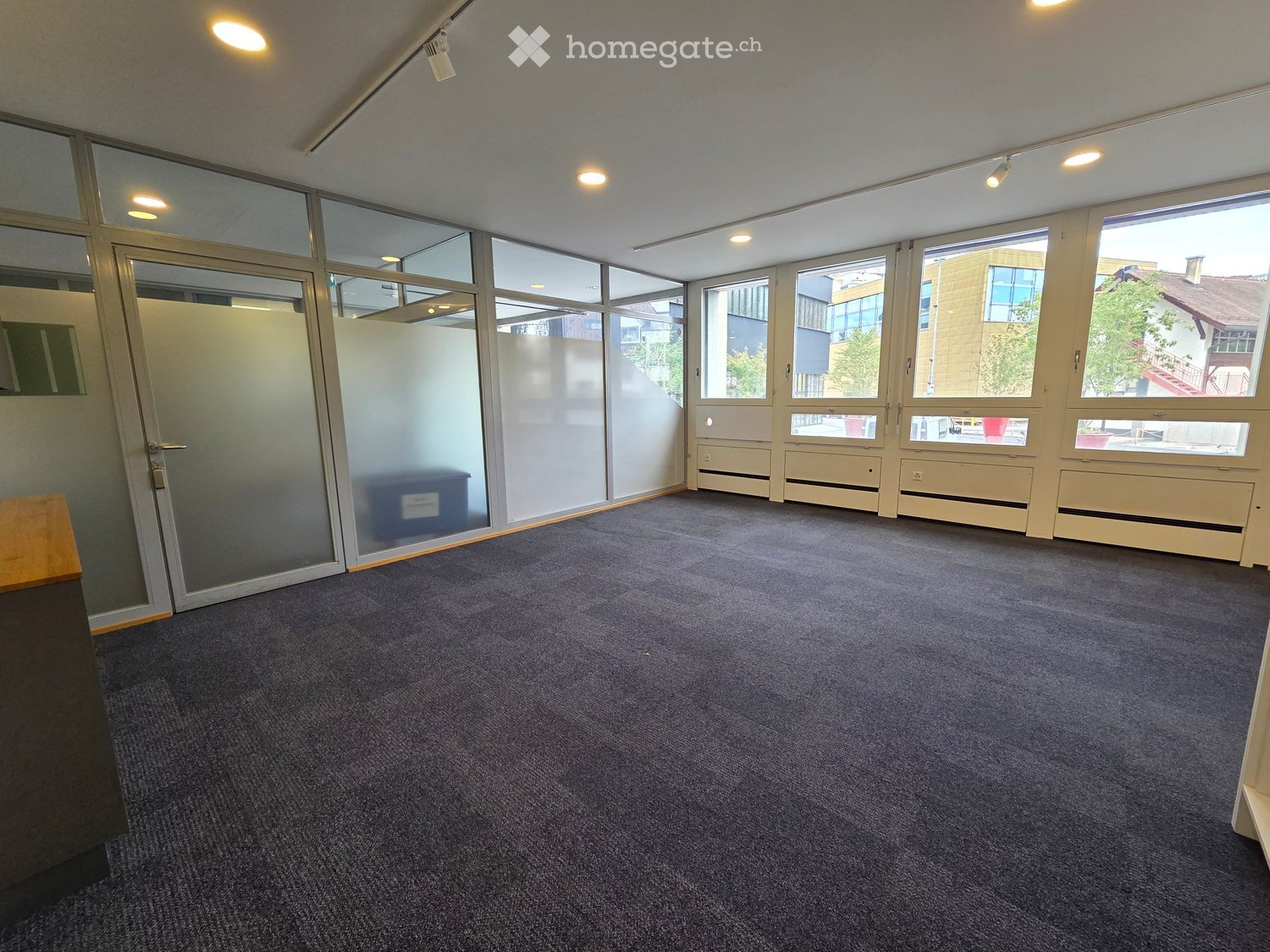 Empty room with carpeted floor, large windows, glass partitions, and recessed lighting.