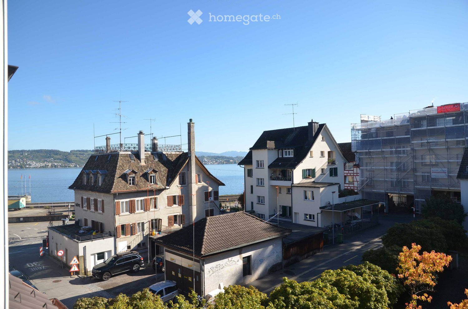 View of a residential area with multiple houses, a lake in the background, and a clear blue sky.