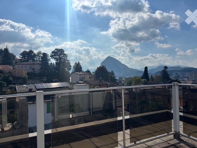 Balcony with a scenic mountain view, modern glass railing, and surrounding houses.