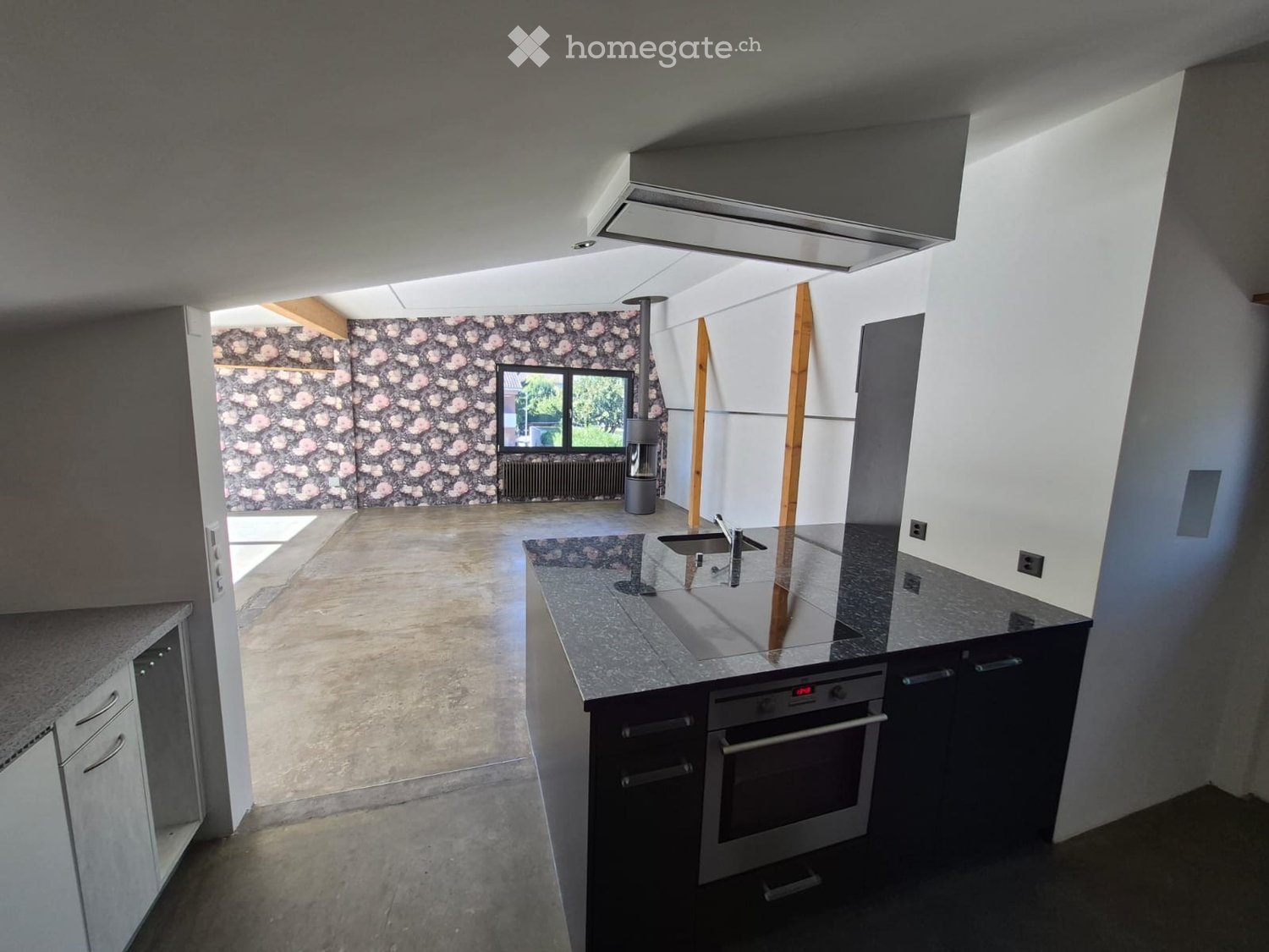 Modern kitchen with granite countertops, stainless steel sink, built-in oven, and dark cabinets. Exposed wooden beams and a large window provide natural light.