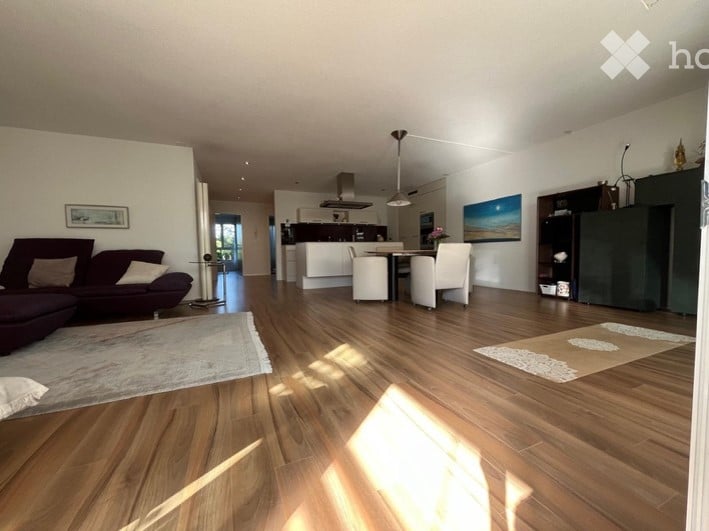 Open-plan living and dining area with hardwood flooring, a dark-colored sofa, a coffee table, dining chairs, a dining table, a kitchen island, and a pendant light fixture.