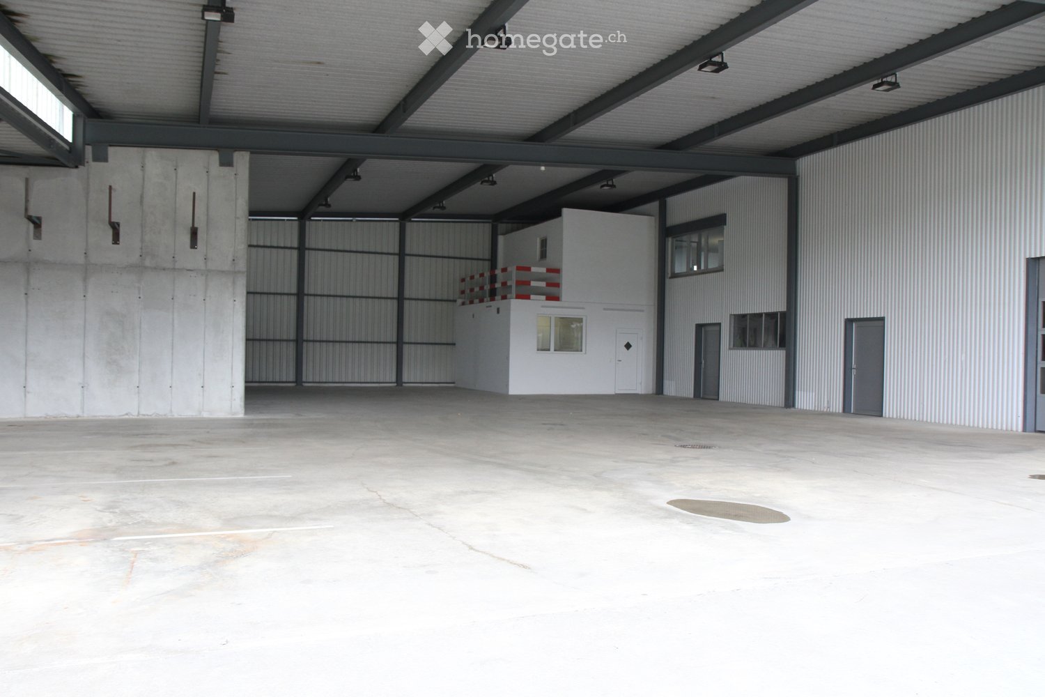 Large industrial warehouse with concrete floors, metal walls, and a raised office area with a balcony overlooking the main space.