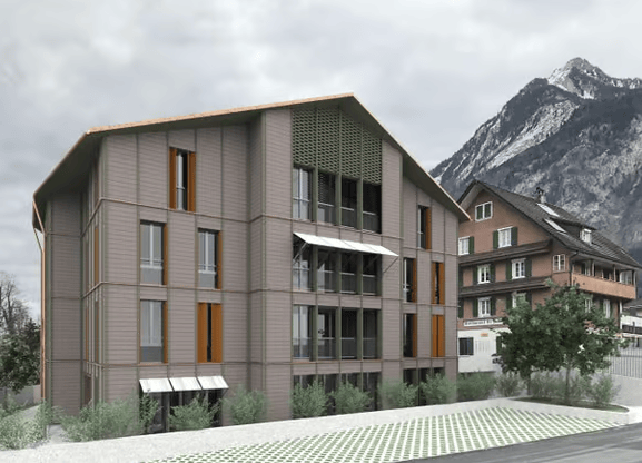 Modern multi-story building with large windows and balconies, situated in a scenic mountainous area with neighboring houses and greenery.