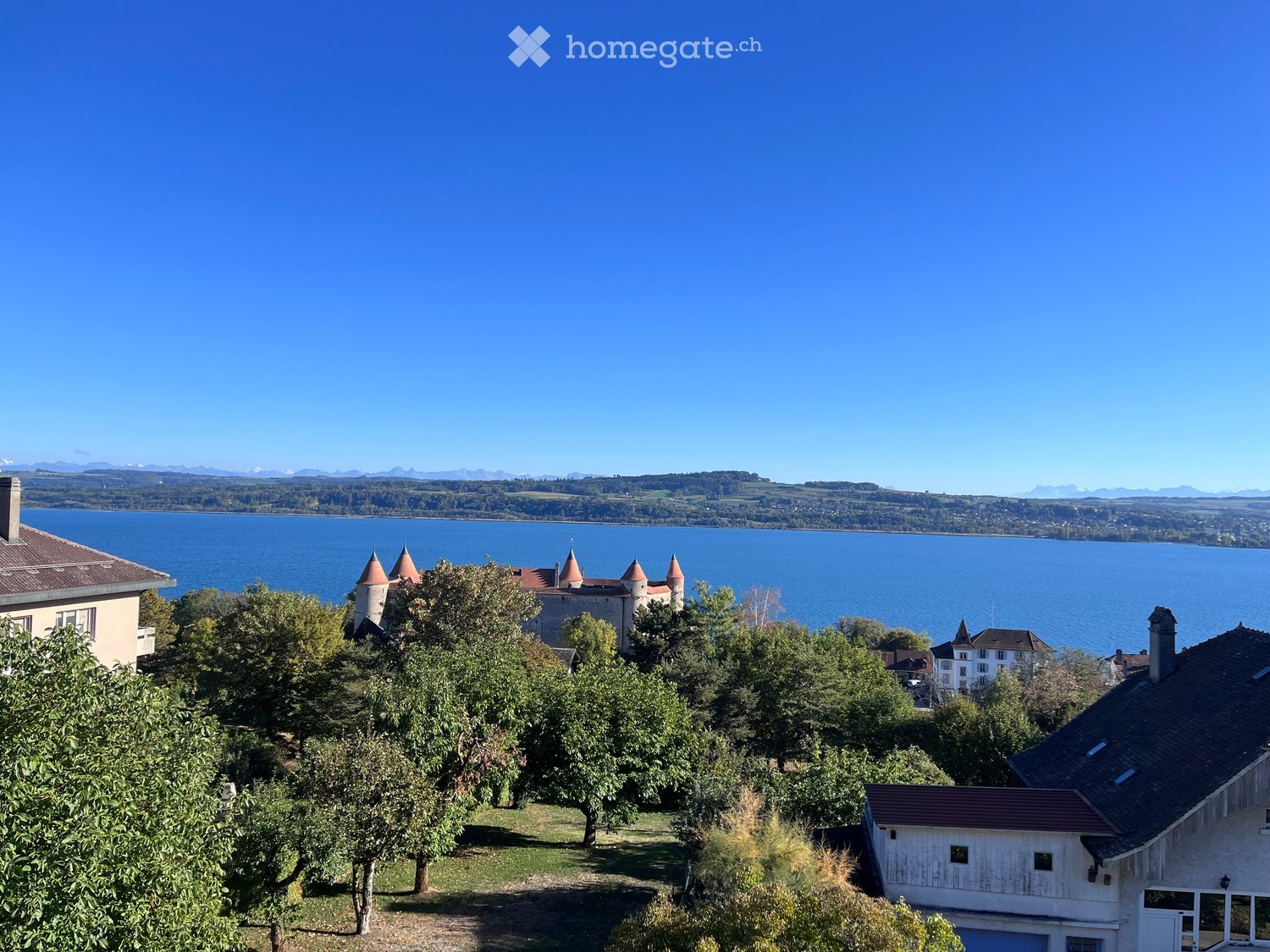A scenic view of a lake with a castle on a hill, surrounded by trees and houses.