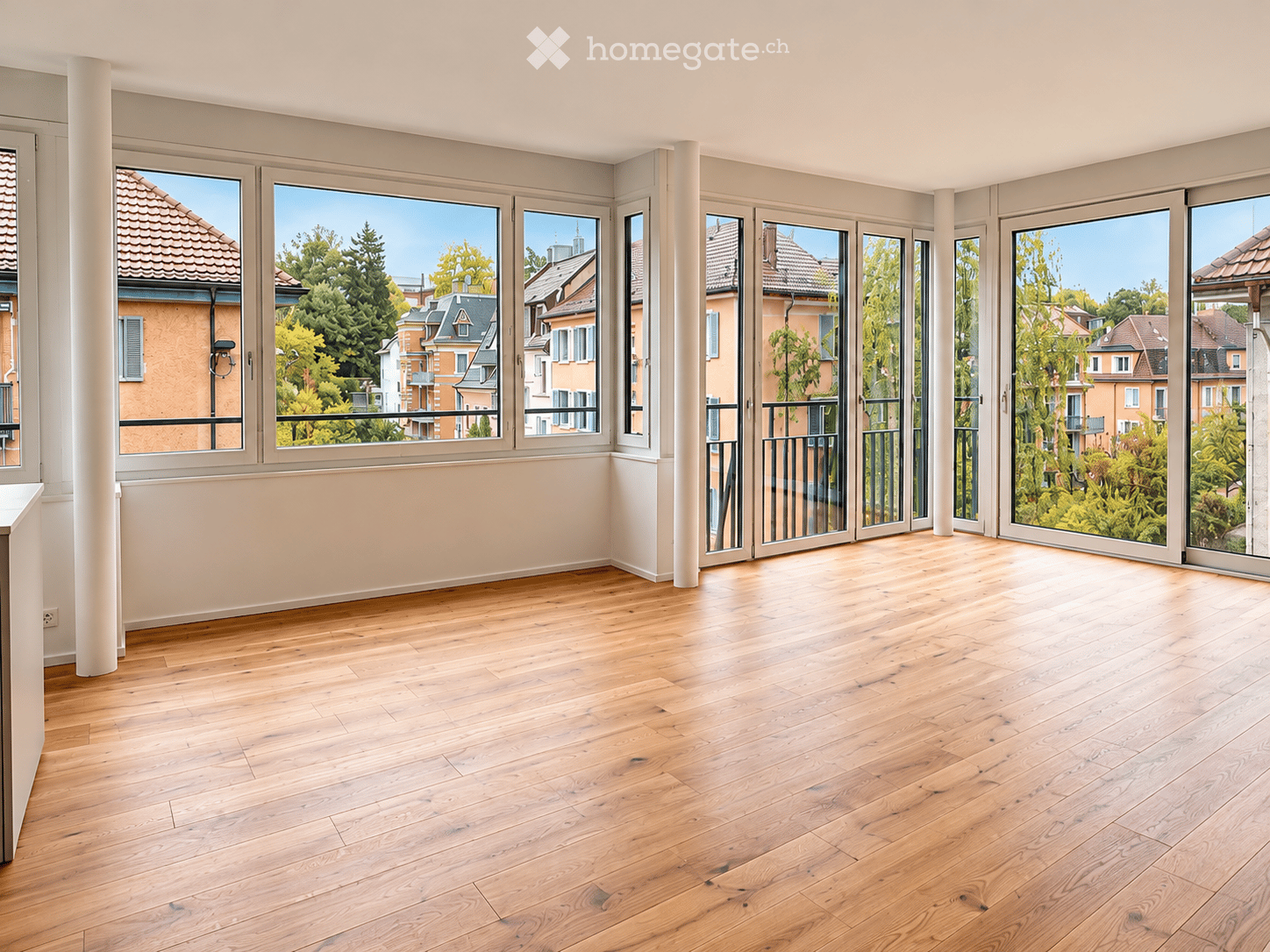 Empty room with wooden flooring, large windows, and sliding glass doors leading to a balcony.