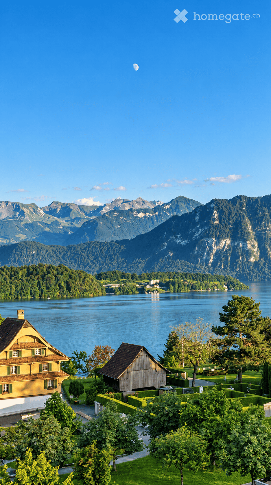 A picturesque view of a Swiss house with a yellow facade and green shutters, situated near a serene lake surrounded by lush greenery and distant mountains.