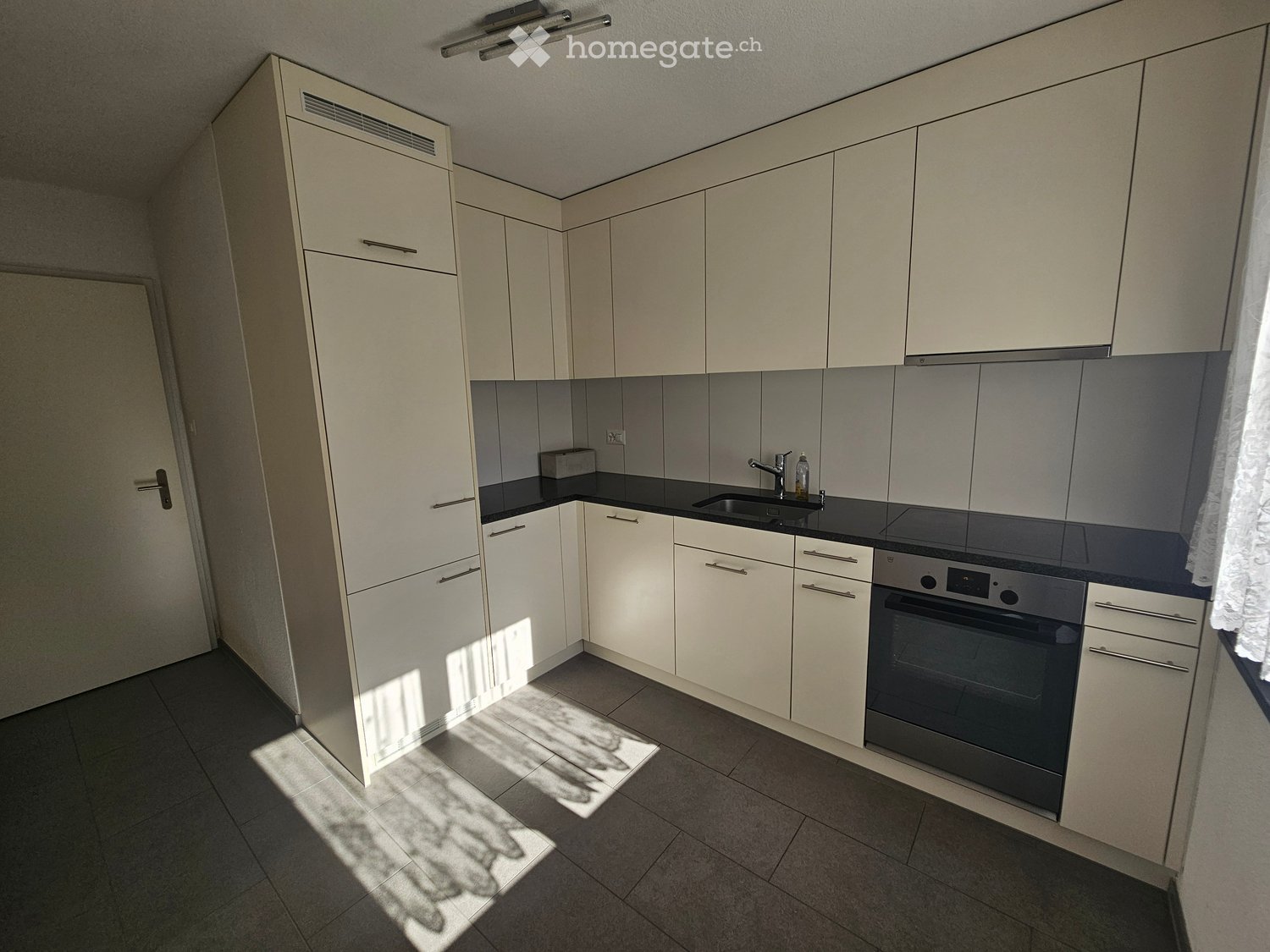 Modern kitchen with white cabinets, dark countertops, and built-in appliances including a sink, oven, and faucet.