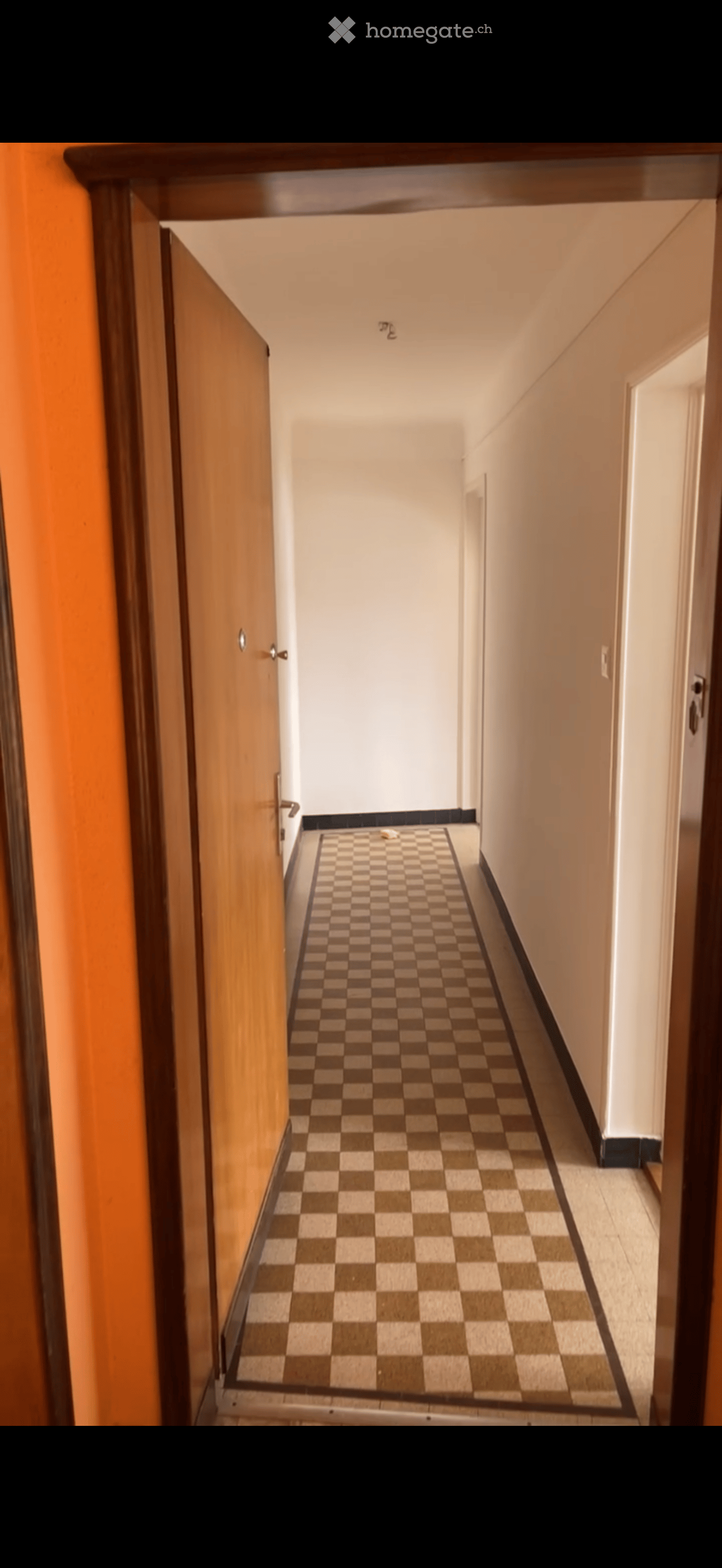 A narrow hallway with a checkered floor, light-colored walls, and wooden doors on both sides.