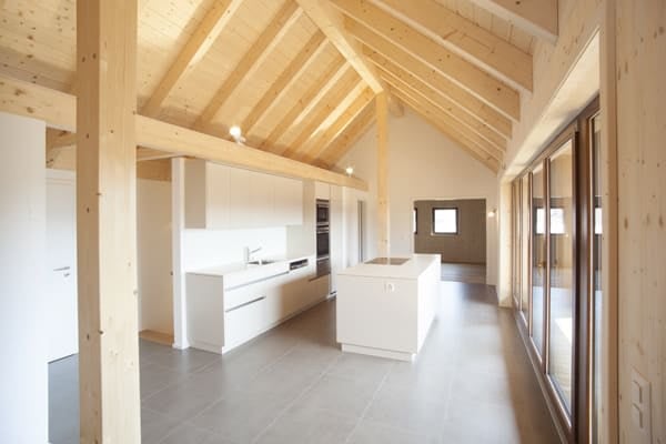 Modern kitchen with white cabinets, a central island, and a sink, featuring exposed wooden beams on the ceiling and large windows.