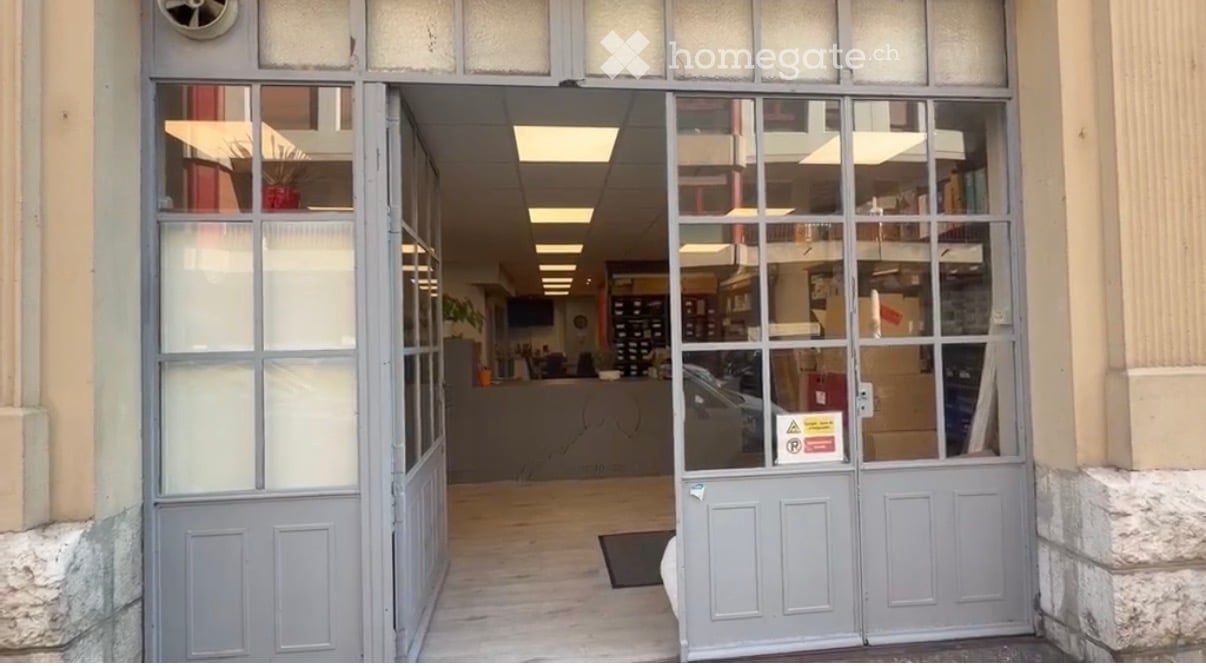 Entrance to a commercial building with glass doors, visible interior showing shelves, desks, and office equipment.