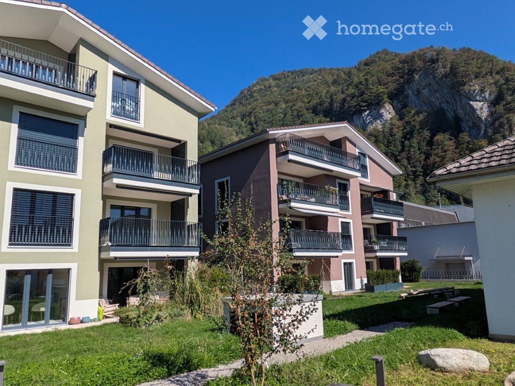 Modern multi-story residential building with balconies overlooking a green lawn and mountain view.