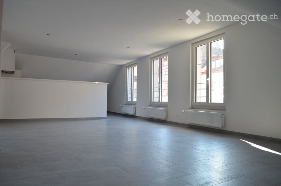 Empty room with light grey walls, large windows, and a smooth tiled floor. No furniture or equipment is present.