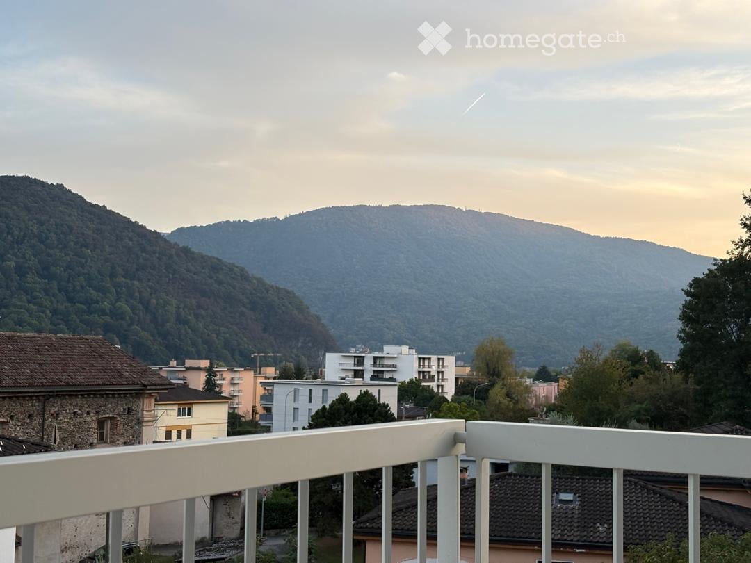 Balcony with white railing overlooking a cityscape and mountains in the background.