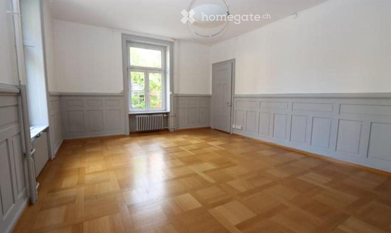 Empty room with wooden flooring, white walls, a window with a radiator below, and a door.