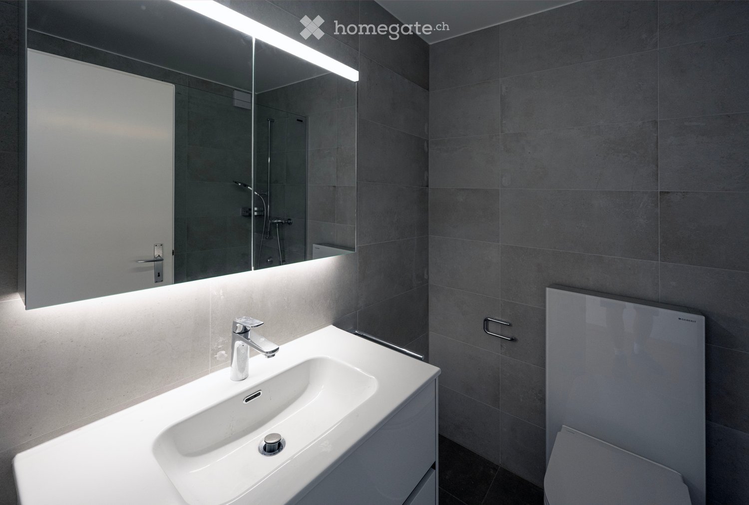 Modern bathroom with a white sink, chrome faucet, large mirror with built-in lighting, and a toilet.