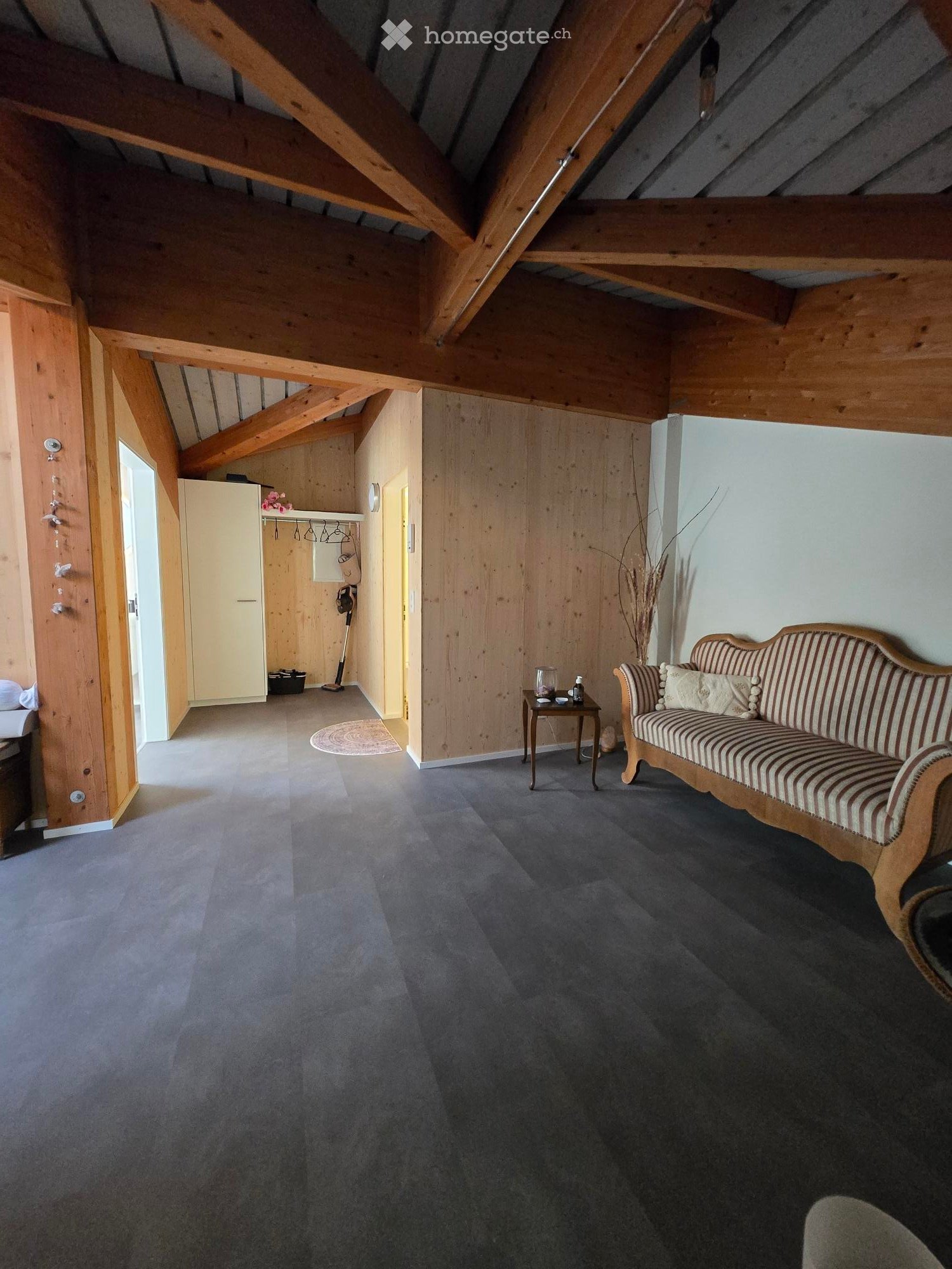 Cozy living room with exposed wooden beams, grey carpet, wooden sofa, small table, and a white wardrobe.