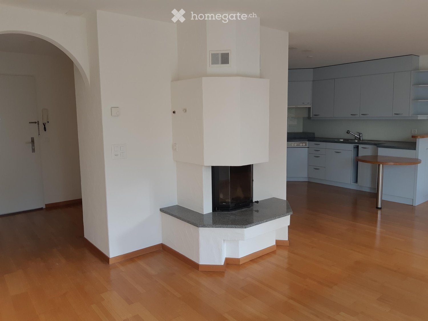 Modern living space with a built-in fireplace, light wooden flooring, and an adjacent kitchen area with cabinets and a sink.